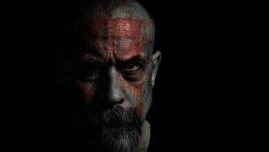 Intense portrait of a bald man with facial tattoos in dark, moody lighting.