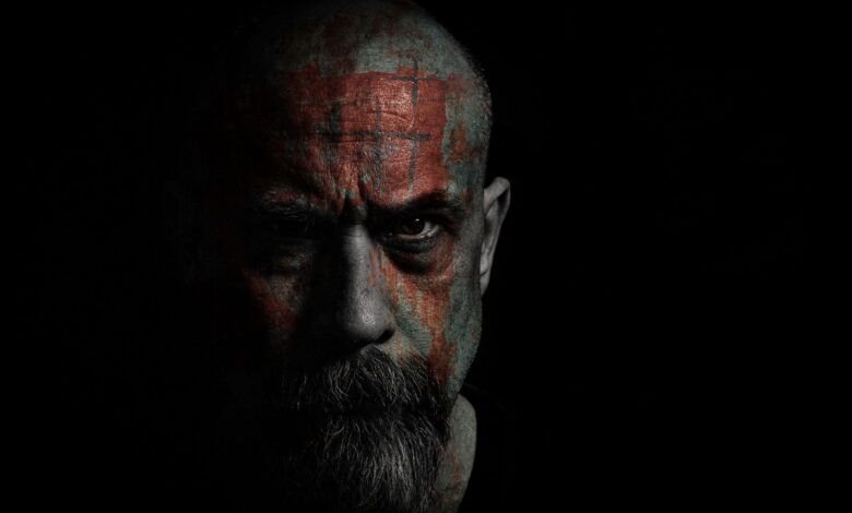 Intense portrait of a bald man with facial tattoos in dark, moody lighting.