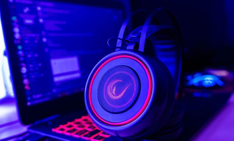 Close-up of gaming headset with neon lighting, placed next to a laptop. Perfect for tech and gaming themes.