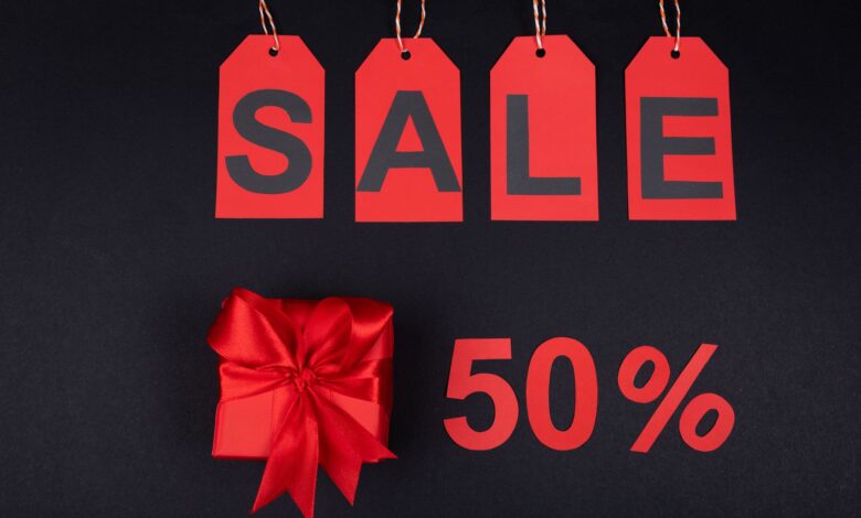 Red gift box next to sale tags and 50% sign on black background, ideal for promotions.