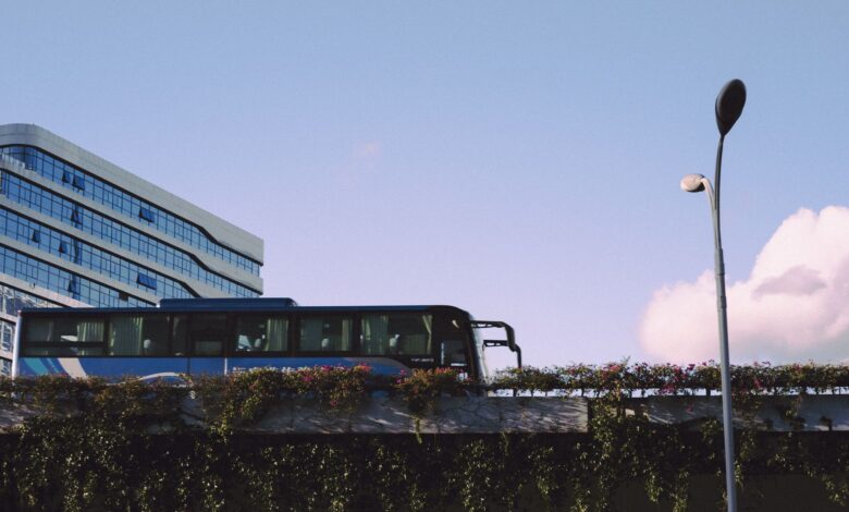 A sleek bus passes by a modern glass building under a bright blue sky.