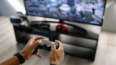 Close-up of hands holding a gaming controller while playing video games indoors.