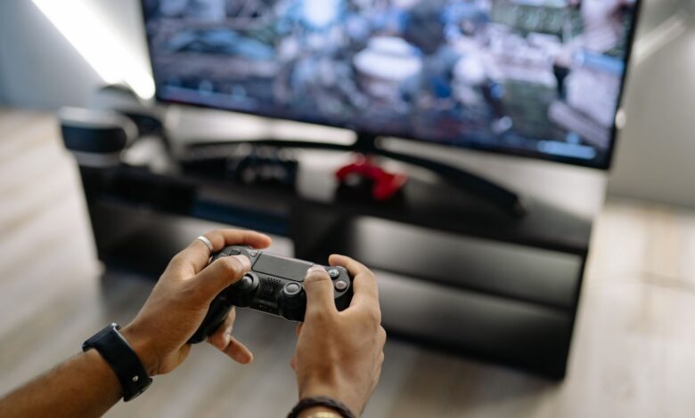 Close-up of hands holding a gaming controller while playing video games indoors.