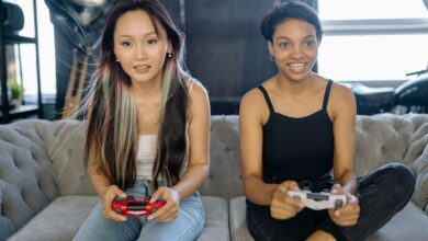 Two women playing video games on a sofa, sharing a fun leisure moment indoors.