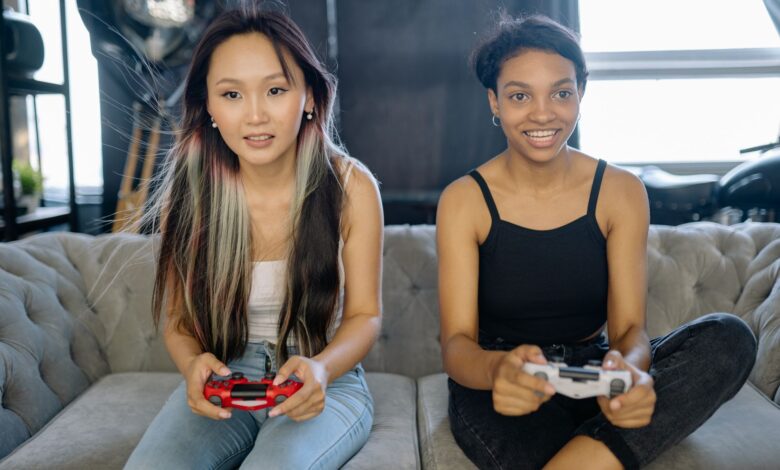 Two women playing video games on a sofa, sharing a fun leisure moment indoors.