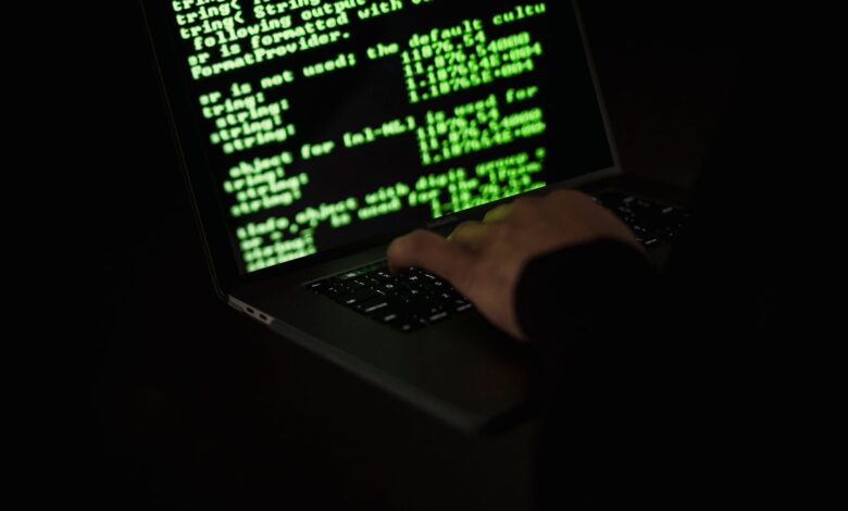 Crop unrecognizable computer geek typing on netbook with codes on screen while hacking system in darkness
