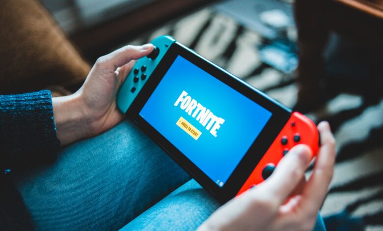 Close-up of hands holding a Nintendo Switch with Fortnite game screen indoors.