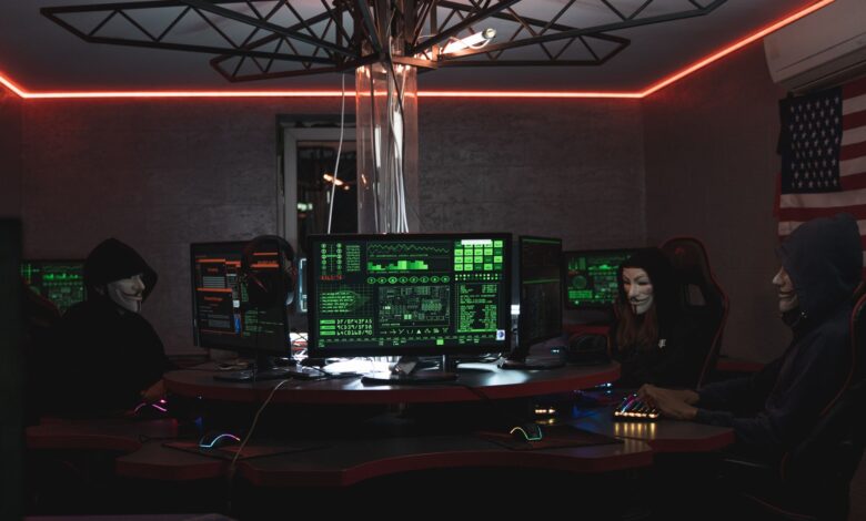 Team of hackers with Guy Fawkes masks coding in a dark room with computers.
