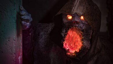 A menacing monster with glowing eyes and mouth in detailed horror cosplay peeking from a shadowy corner.