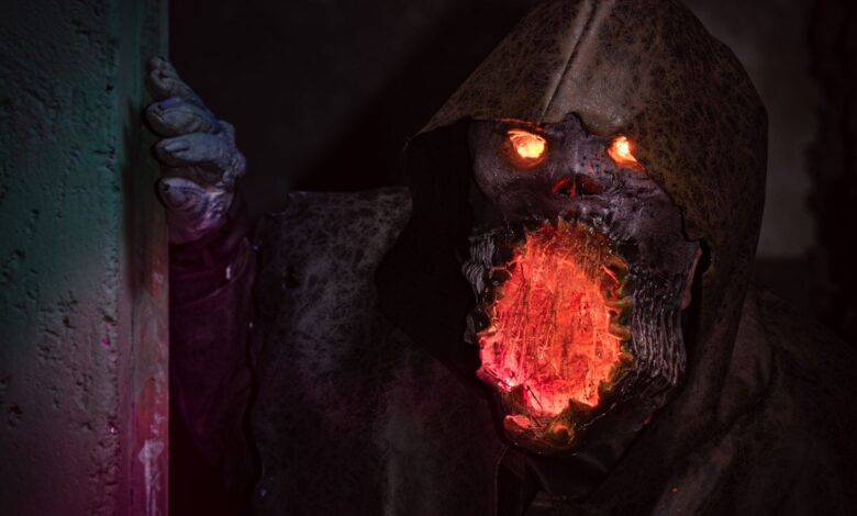 A menacing monster with glowing eyes and mouth in detailed horror cosplay peeking from a shadowy corner.