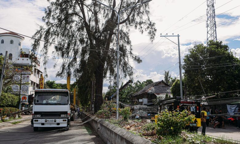 Street view of a truck near fallen power lines with trees and buildings.
