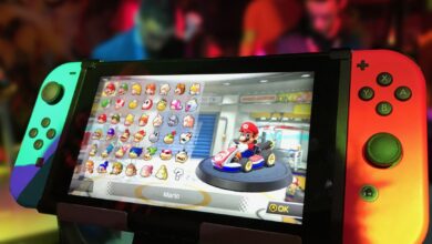 Close-up of a Nintendo Switch showing Mario Kart selection screen, gaming atmosphere in the background.