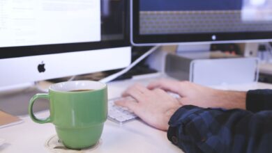 Person typing at a desk with coffee and computer screens. Perfect for business or technology themes.