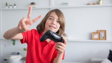 Young boy in a red polo shirt playing video games and flashing a peace sign indoors.