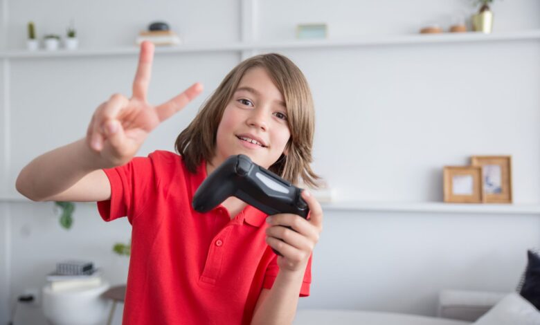 Young boy in a red polo shirt playing video games and flashing a peace sign indoors.