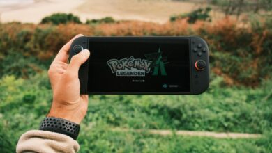 A person holds a handheld gaming device outdoors with Pokémon Legends on screen.