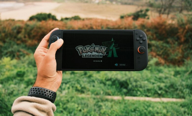 A person holds a handheld gaming device outdoors with Pokémon Legends on screen.