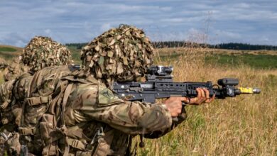 Military soldiers in camouflage gear practicing combat in a grassy countryside.