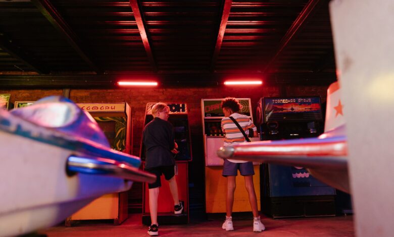 Teenagers playing classic arcade games in a dimly lit amusement arcade, embracing a retro vibe.
