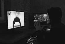 Monochrome image of a masked hacker on a video call, showcasing cyber security themes.