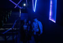 Young adults entering a dimly lit movie theater, holding popcorn with neon blue lighting.