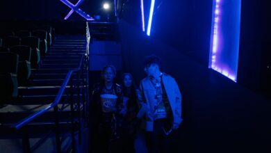 Young adults entering a dimly lit movie theater, holding popcorn with neon blue lighting.