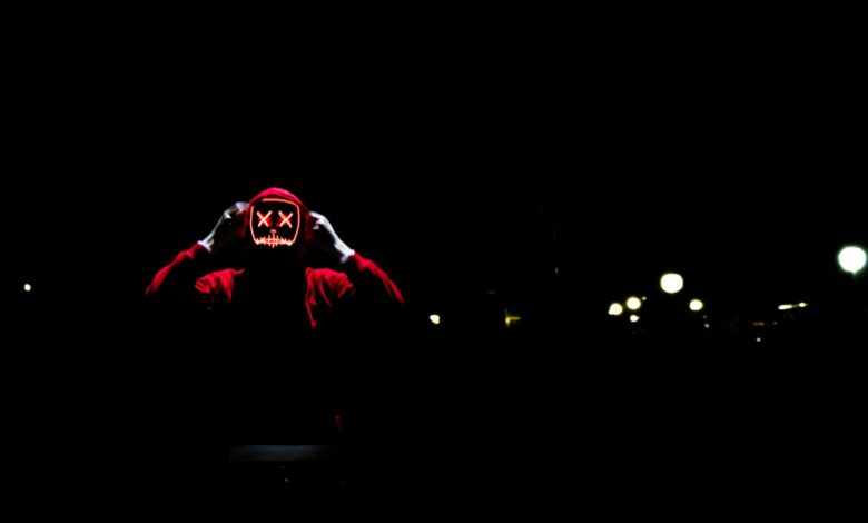 A spooky figure wearing a glowing LED mask in the darkness, perfect for Halloween themes.