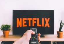 A hand holding a TV remote in front of a screen with Netflix, perfect for streaming and movie night themes.