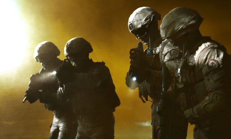 Four soldiers in tactical gear advancing in a smoky battlefield setting.