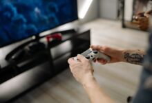 Person playing video games using a game controller indoors on a modern TV setup.