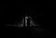A shadowy figure explores a dimly lit, eerie attic with a flashlight.
