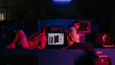 Teenagers play video games in a neon-lit setting with vintage monitors, capturing a retro aesthetic.