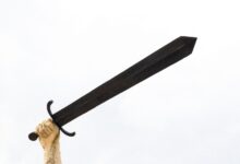 A stone sculpture hand holding a large sword against a bright sky, symbolizing power and strength.