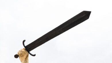 A stone sculpture hand holding a large sword against a bright sky, symbolizing power and strength.