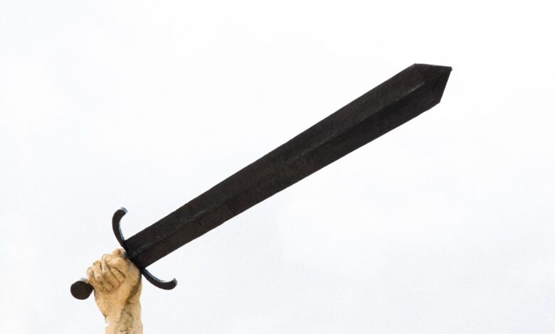 A stone sculpture hand holding a large sword against a bright sky, symbolizing power and strength.
