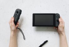 Close-up of hands holding a Nintendo Switch and Joy-Con controllers on a white surface.