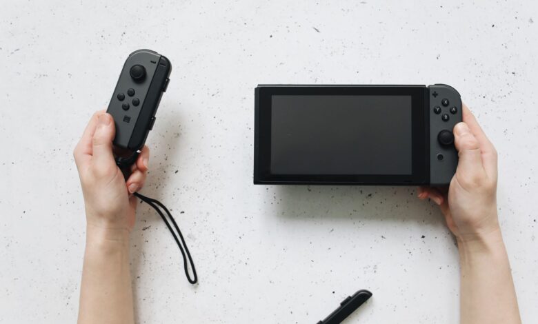 Close-up of hands holding a Nintendo Switch and Joy-Con controllers on a white surface.
