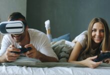 A couple lying on a bed, having fun with virtual reality and gaming consoles.
