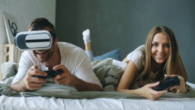 A couple lying on a bed, having fun with virtual reality and gaming consoles.