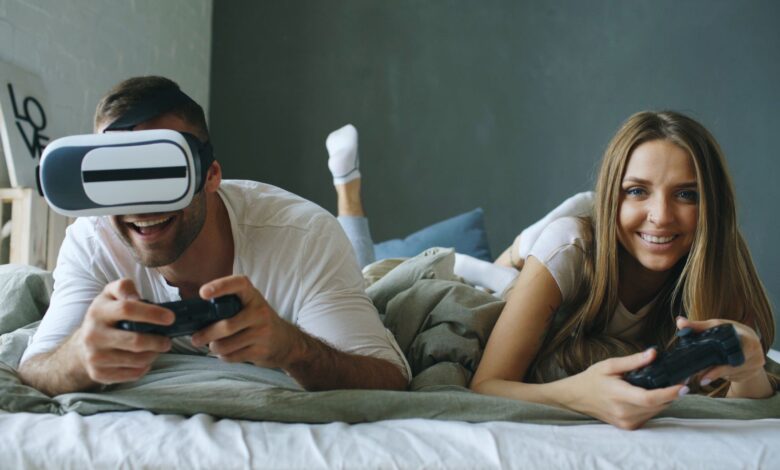 A couple lying on a bed, having fun with virtual reality and gaming consoles.