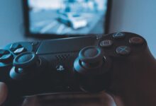 A hand holding a wireless game controller in front of a blurry screen, capturing the gaming experience.