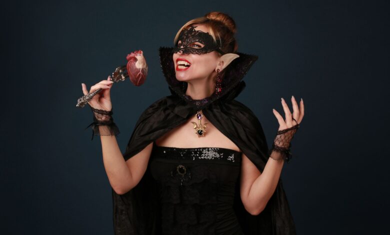 A woman dressed as a vampire enjoying Halloween with a heart prop in hand.