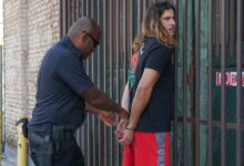Police officer handcuffing a suspect during an arrest against an urban backdrop.