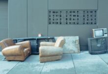 Sidewalk scene with vintage chairs and old televisions against a wall.