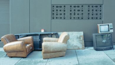 Sidewalk scene with vintage chairs and old televisions against a wall.