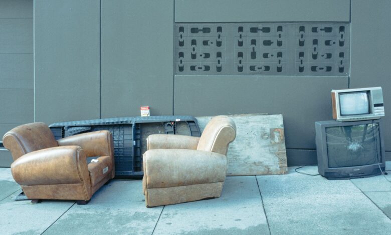 Sidewalk scene with vintage chairs and old televisions against a wall.