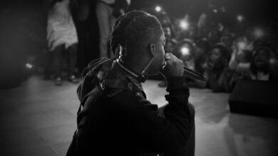 Side view of black and white unrecognizable African American singer with dreadlocks performing song on stage with microphone in hand during concert