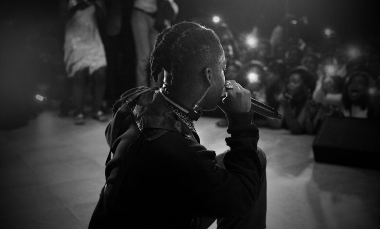 Side view of black and white unrecognizable African American singer with dreadlocks performing song on stage with microphone in hand during concert