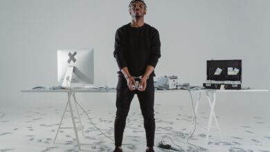 A handcuffed man stands in a room with scattered money, a computer, and a briefcase.