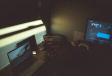 Dark room with a laptop and gaming console creating a moody tech atmosphere.